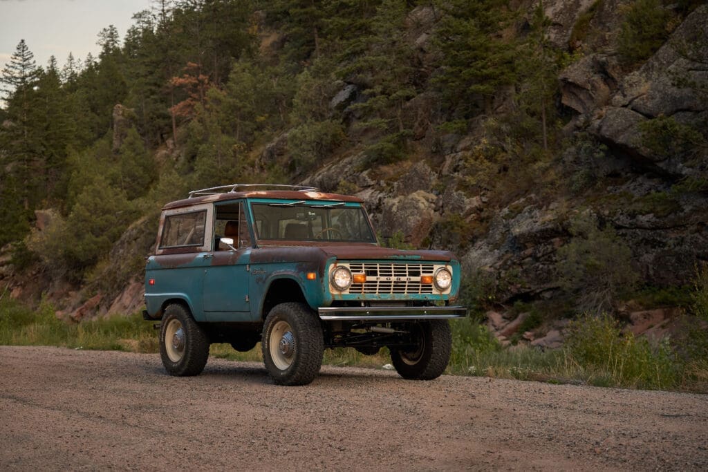 1973 Classic Ford Bronco Patina parked on a mountain road with rugged natural surroundings. The original weathered finish, vintage details, and lifted stance highlight this unrestored Bronco’s authentic character and Classic Ford Broncos’ dedication to preserving the timeless heritage of early-generation off-road vehicles.