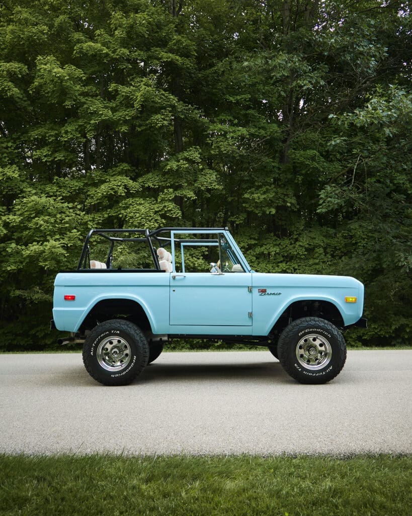1976 Classic Ford Bronco parked on a quiet tree-lined road with lifted suspension, roll cage, and BFGoodrich All-Terrain tires. This restored vintage Ford Bronco highlights Classic Ford Broncos’ expert craftsmanship and modern performance upgrades while preserving the timeless appeal of the original first-generation design.