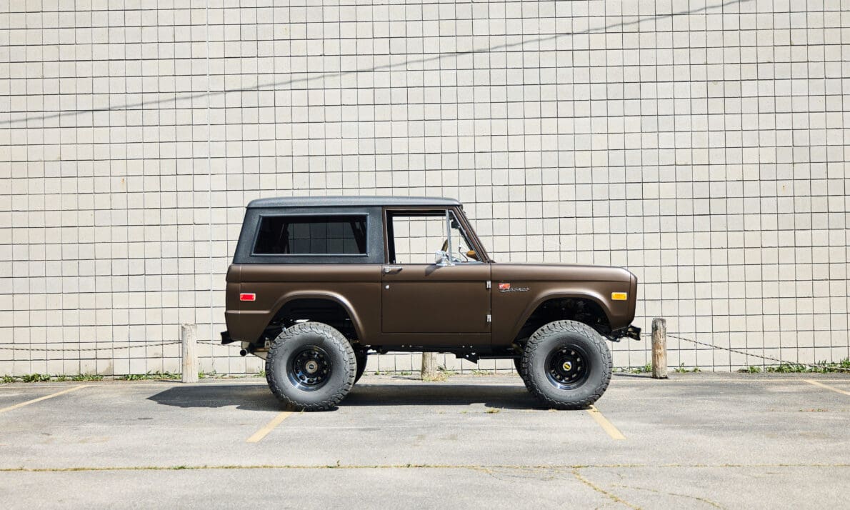 Brown Classic Ford Bronco with black hardtop, lifted suspension, and rugged off-road tires shown in clean side profile, highlighting vintage 4x4 design and restored craftsmanship.